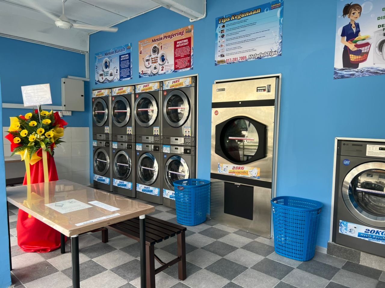 Blue-walled laundromat with stacked washer-dryers, a large front-load washer and a folding table